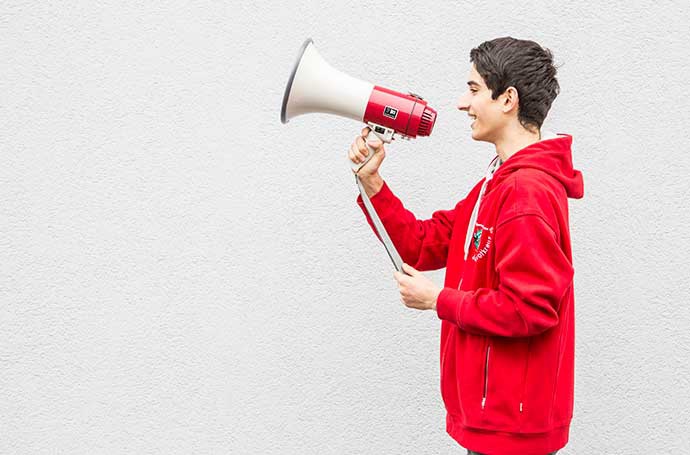 Auf der Suche nach Materialien und Informationen? Hier ist man an der richtigen Stelle! Beim JRK steht der Service ganz weit vorn! JRK-Team ©BJRK Ein Jugendrotkreuzler hält ein Megaphon in der Hand.